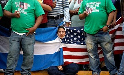 Giovane salvadoregna si avvolge con la bandiera di Stati Uniti e El Salvador in una manifestazione di protesta contro misure antimmigrazione. Foto AFP/Chip Somodevilla